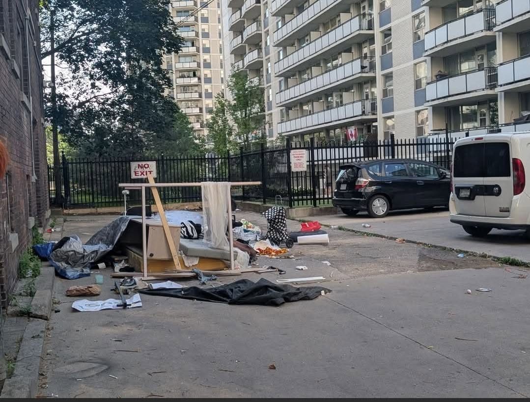 Abandoned furniture, tarps and debris piled in a Toronto Centre laneway in front of residential towers